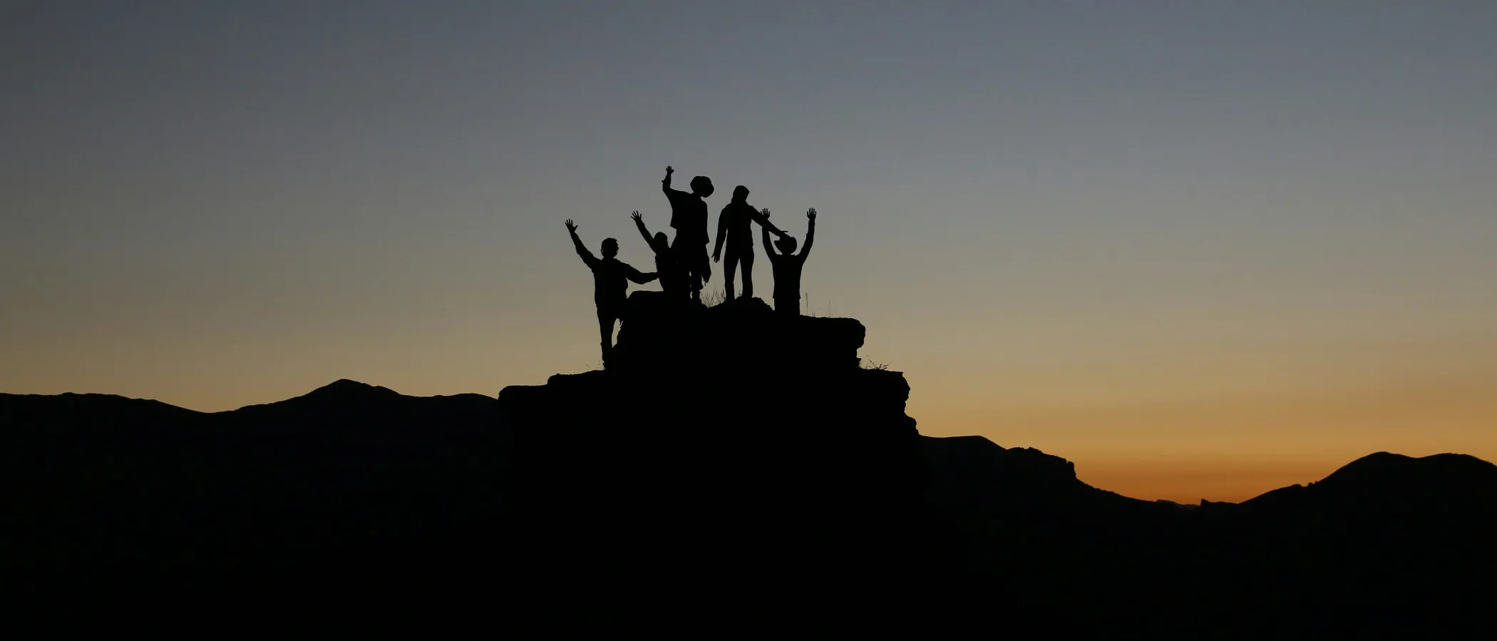 Team-Silhouetten im Abendlicht auf einem Gipfel
